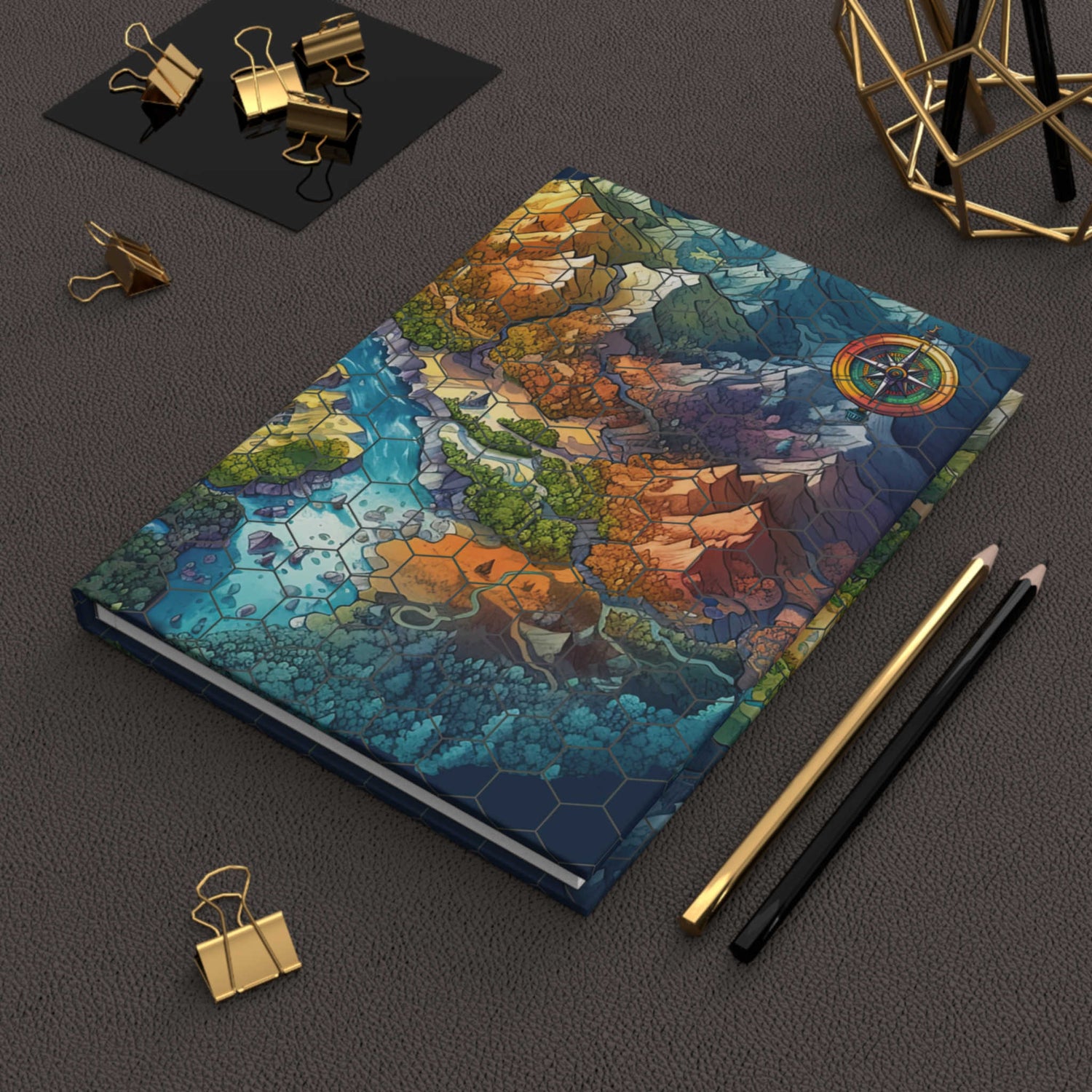 Image depicts a hardcover journal sitting on top of a desk. Journal design features a colorful fantasy map with an octagon overlay and a compass marker in the upper right.